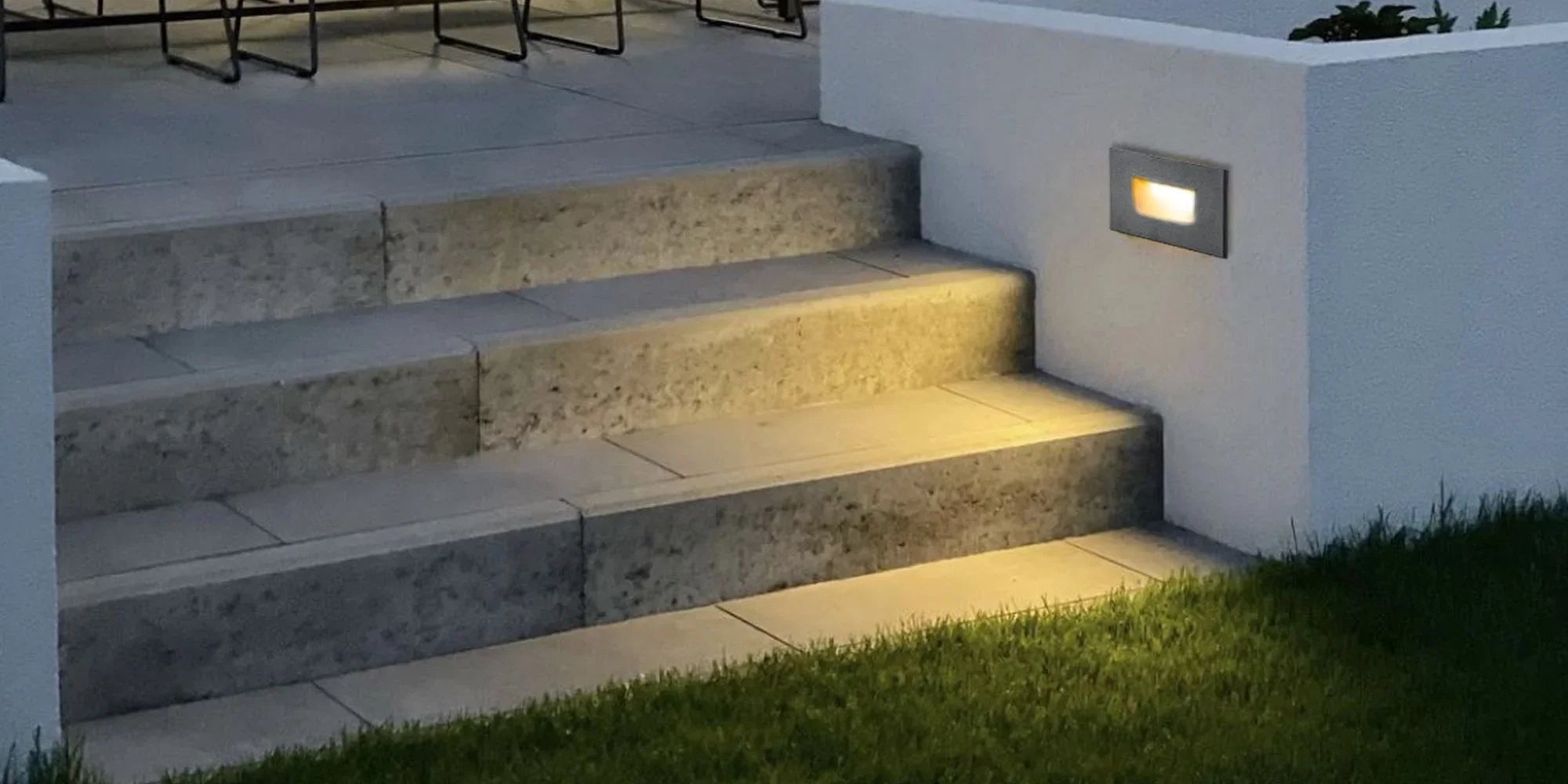 Outdoor LED wall light illuminating modern patio steps at dusk